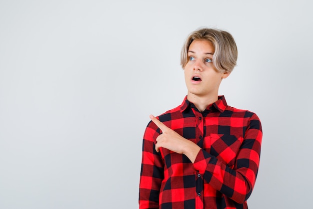 Young teen boy pointing at upper left corner, looking up in checked shirt and looking wondered. front view.