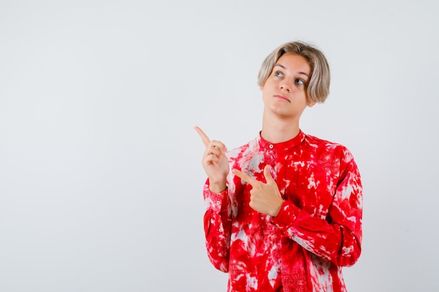 Young teen boy pointing at upper left corner in shirt and looking focused , front view.