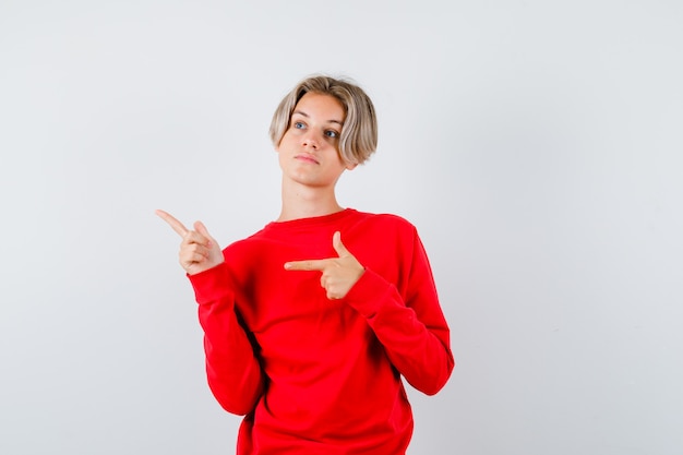 Young teen boy in red sweater pointing at upper left corner, looking away and looking pensive , front view.