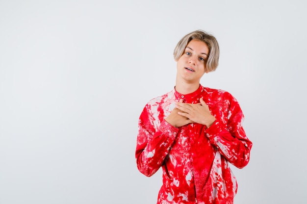 Giovane ragazzo adolescente in camicia con le mani sul petto e guardando grato, vista frontale.