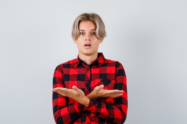 Foto giovane ragazzo adolescente che mostra entrambi i lati in camicia a quadri e sembra confuso. vista frontale.