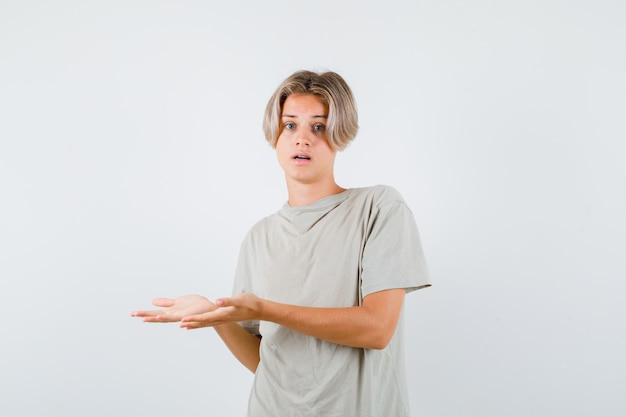 Young teen boy showing welcoming gesture in t-shirt and looking puzzled