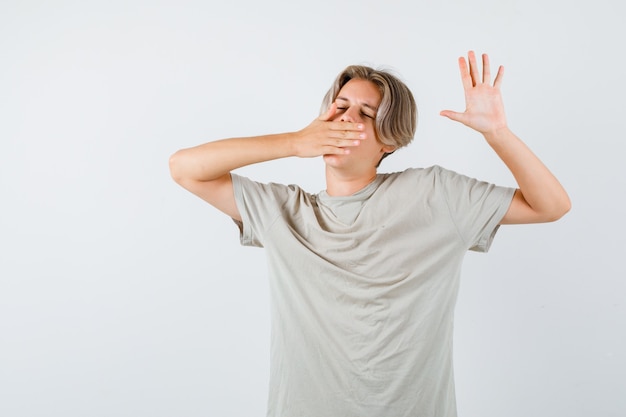 Young teen boy in t-shirt yawning and stretching upper body and looking sleepy