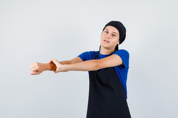 Young teen cook stretching arms in t-shirt, apron and looking relaxed. front view.