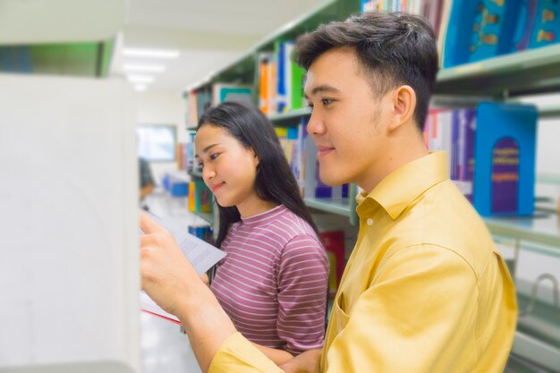 Young teen people read and talk open book at bookshelf.