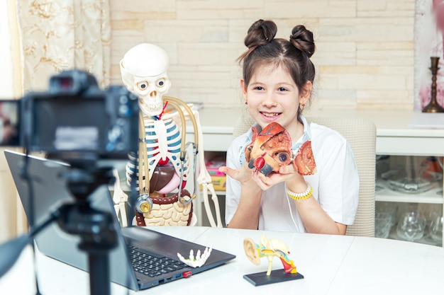 Young teenage girl is recording a video blog at home. She tells subscribers about human anatomy. Unusual hobby.