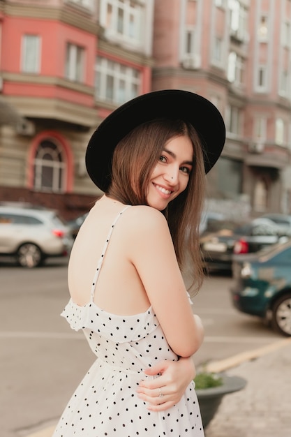 Young teenage girl in a white dress and hat posing in the city