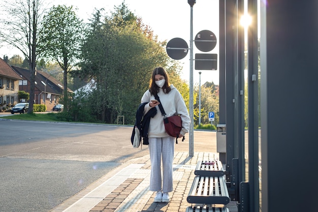 A young teenage woman is waiting for a bus at a bus stop early in the morning