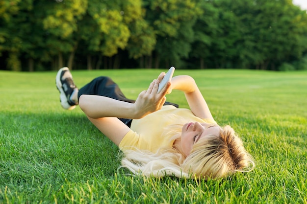 Young teenage woman lying on green grass using smartphone