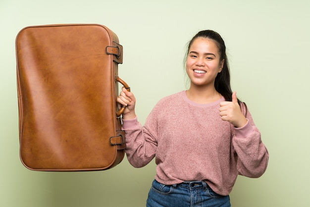 ビンテージブリーフケースを保持している孤立した緑の背景の上の若い10代のアジアの女の子