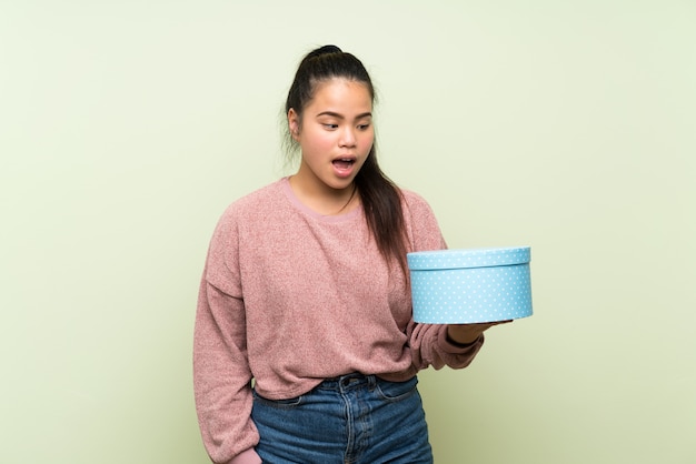 Young teenager Asian girl over isolated green wall holding gift box