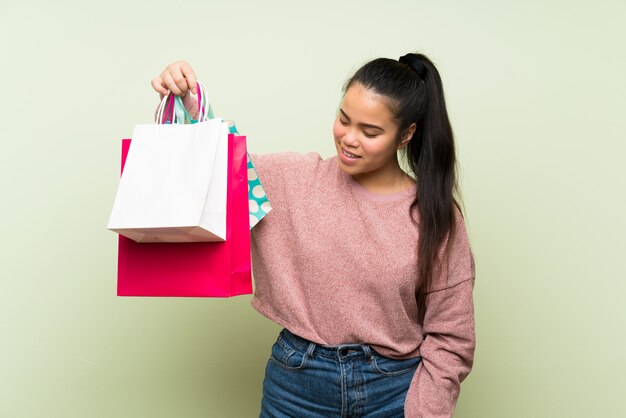 多くの買い物袋を保持している孤立した緑の壁の上の若い10代のアジアの女の子