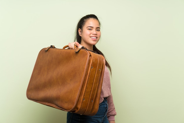 Young teenager Asian girl over isolated green wall holding a vintage briefcase