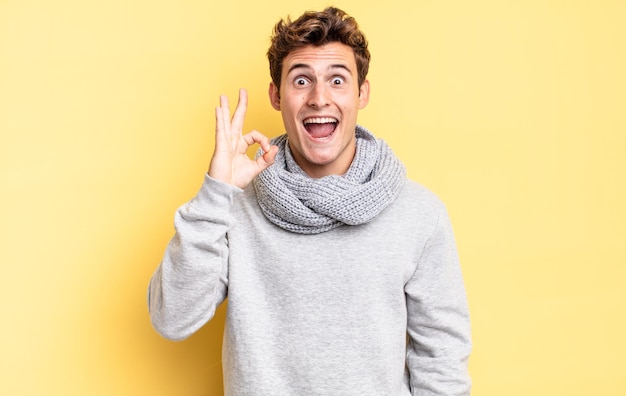 Young teenager boy feeling successful and satisfied, smiling with mouth wide open, making okay sign with hand