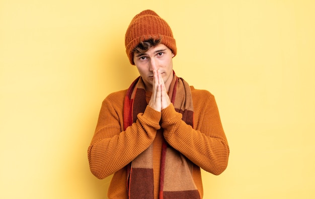 Young teenager boy feeling worried, hopeful and religious, praying faithfully with palms pressed, begging forgiveness