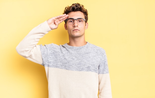 Young teenager boy greeting the camera with a military salute in an act of honor and patriotism, showing respect