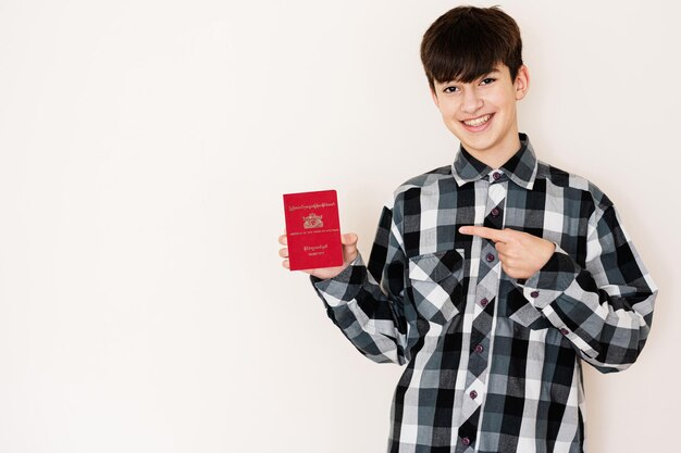 Young teenager boy holding Myanmar passport looking positive and happy standing and smiling with a confident smile against white background