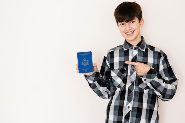 Young teenager boy holding San Marino passport looking positive and happy standing and smiling with a confident smile against white background