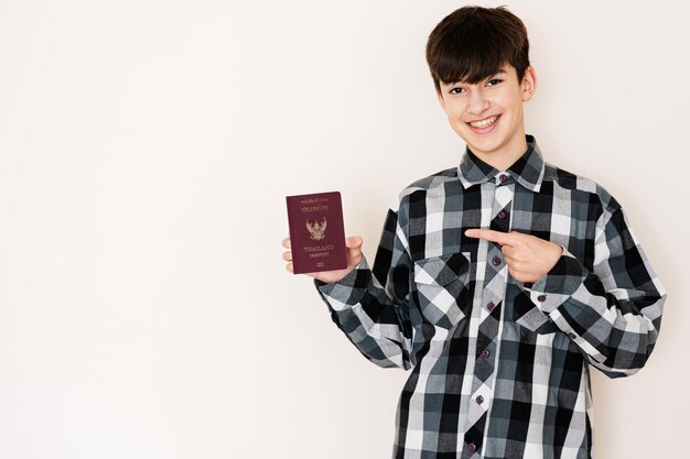 Young teenager boy holding Thailand passport looking positive and happy standing and smiling with a confident smile against white background