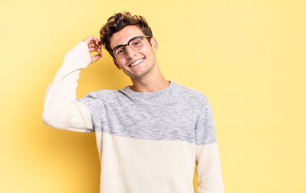 Young teenager boy smiling cheerfully and casually, taking hand to head with a positive, happy and confident look