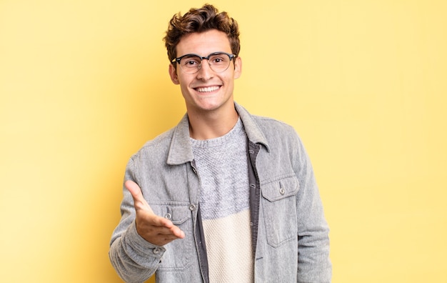 Young teenager boy smiling, looking happy, confident and friendly, offering a handshake to close a deal, cooperating