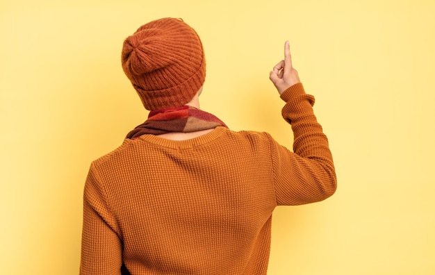 Young teenager boy standing and pointing to object on copy space, rear view