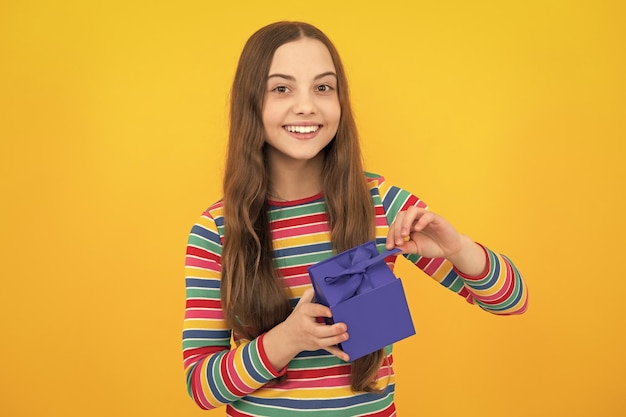 Young teenager girl child holding gift box isolated on yellow background Gift for kids birthday