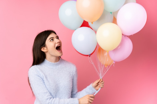 Young  teenager girl holding lots of balloons over pink wall