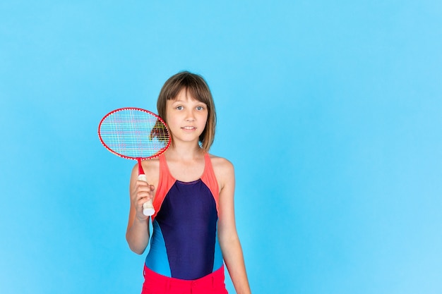 Young teenager girl jumping and playing badminton on blue wall