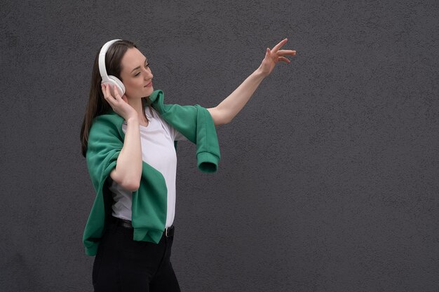 A young teenager girl listens to music with headphones dressed in a black jacket and jeans