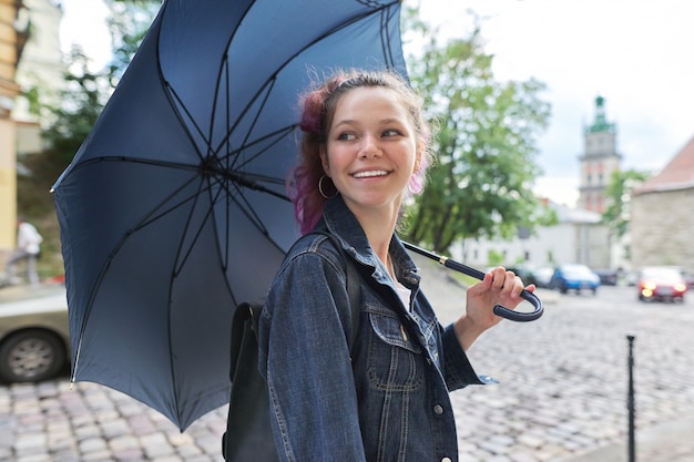 Young teenager girl under an umbrella on the street of city