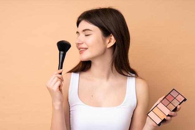 Young  teenager girl over wall with makeup palette and happy