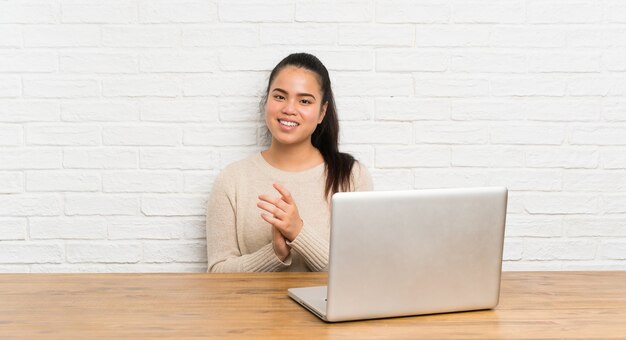 Young teenager girl with a laptop in a table applauding