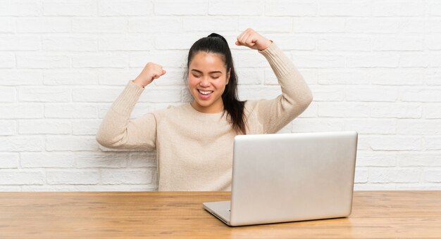 Young teenager girl with a laptop in a table celebrating a victory