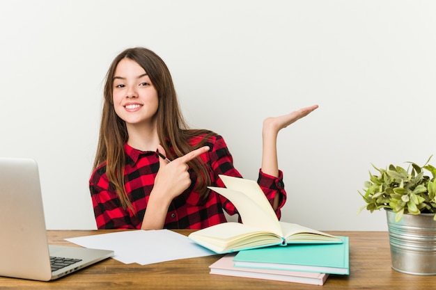 Young teenager going back to her routine doing homeworks excited holding a copy space on palm.