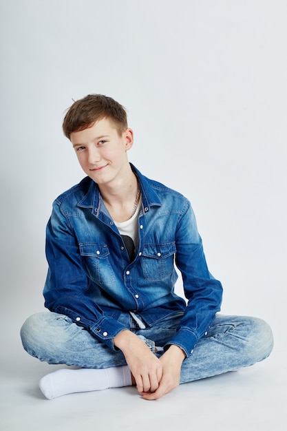 Young teenager guy sits in blue jeans on the floor