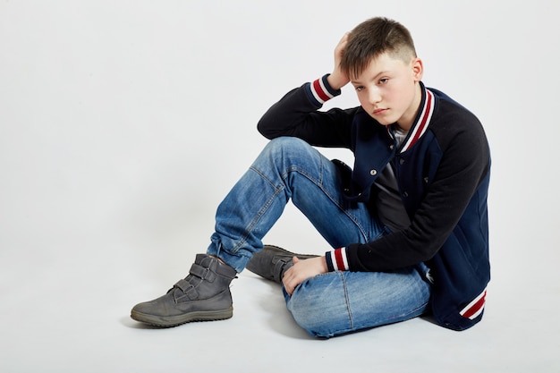 Young teenager guy sits in blue jeans on the floor