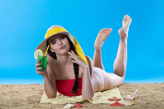 A young teenager is lying on the beach with an alcoholic drink and sunbathing in the summer sun