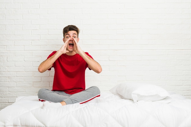 Young teenager student man on the bed shouting excited to front.