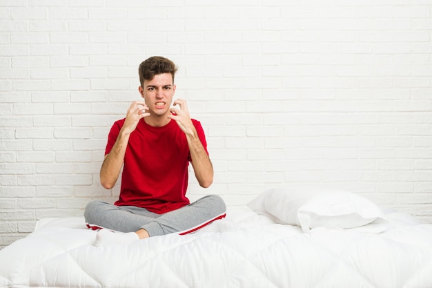 Young teenager student man on the bed upset screaming with tense hands.