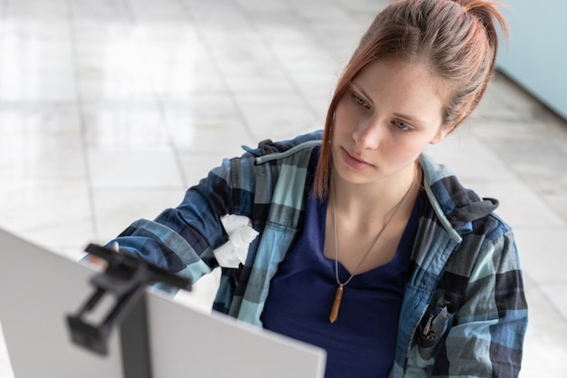 Young teenager woman artist paints with oil paints sitting on the marble floor. White canvas and easel stand on the floor of marble tiles in the room with turquoise and light green walls.