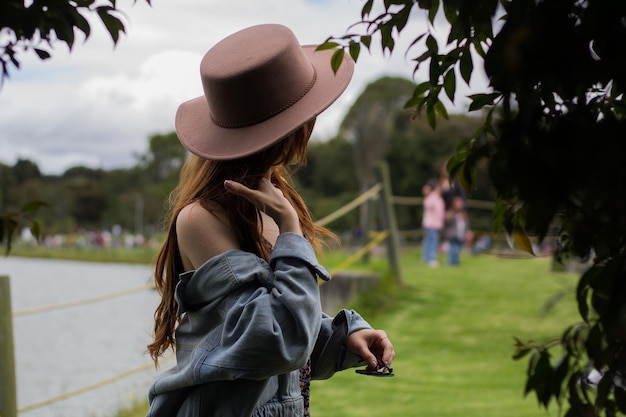 Young teenager woman wearing a hat sitting on the grass near the lake river meditating relaxing