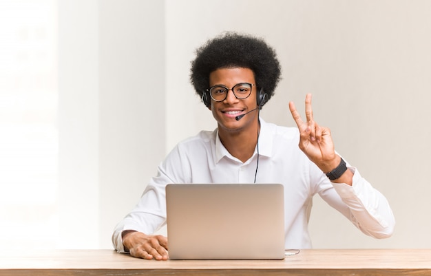 Giovane uomo di colore telemarketer divertente e felice facendo un gesto di vittoria