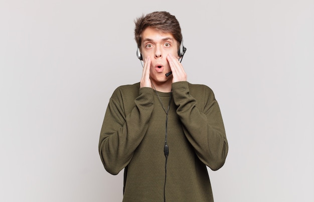 Young telemarketer feeling shocked and scared, looking terrified with open mouth and hands on cheeks