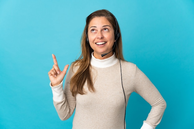 Young telemarketer woman over isolated blue wall thinking an idea pointing the finger up