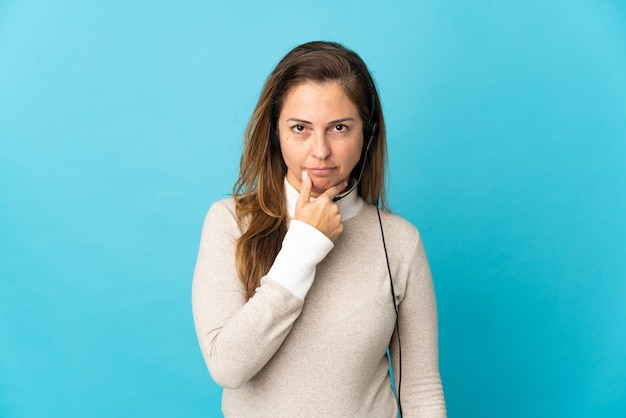 Young telemarketer woman over isolated blue wall thinking