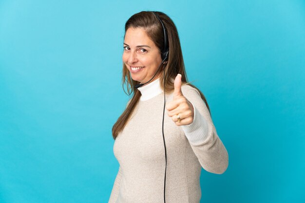 Young telemarketer woman over isolated blue wall with thumbs up because something good has happened