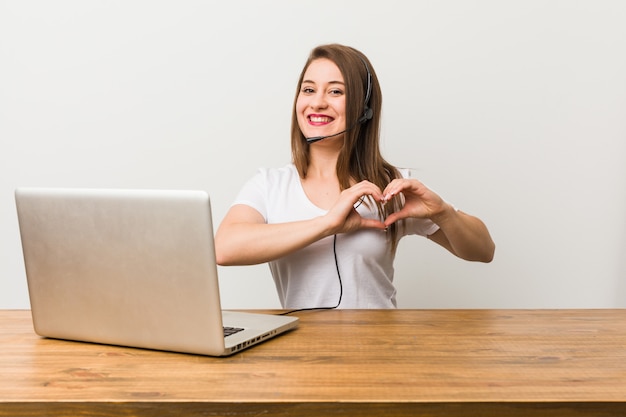 Young telemarketer woman smiling and showing a heart shape with hands