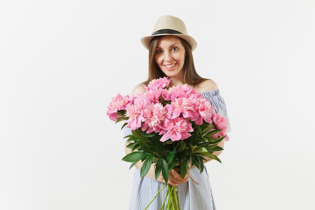 青いドレス、白い背景で隔離の美しいピンクの牡丹の花の花束を保持している帽子の若い優しい女性。聖バレンタインの日、国際女性の日の休日の概念。広告エリア。