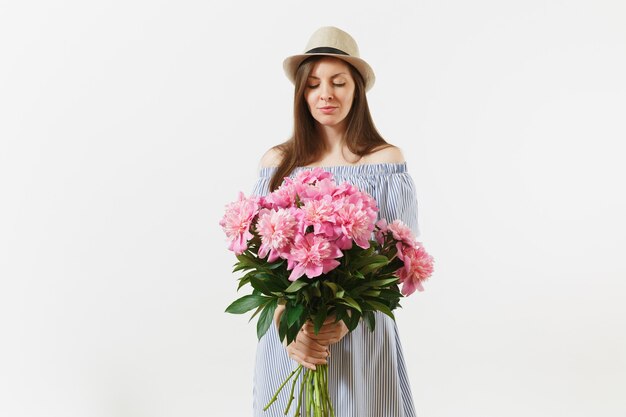 青いドレス、白い背景で隔離の美しいピンクの牡丹の花の花束を保持している帽子の若い優しい女性。聖バレンタインの日、国際女性の日の休日の概念。広告エリア。